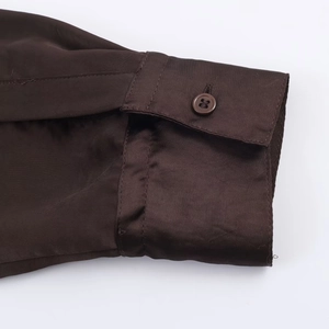 Dettaglio del polsino della camicia in raso marrone con trama in seta e bottone coordinato