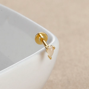 Vue macro d'un piercing labret doré avec opale en forme de poire sur bord céramique