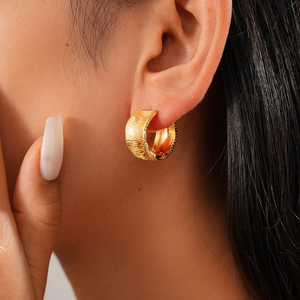 Close-up of 18K gold plated hoop earrings with textured feather stripes on female model