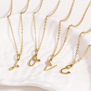 Golden stainless steel heart necklaces with cursive initial pendants J, O, V, E on shell tray