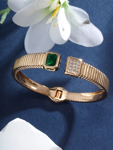 Close-up of gold open bangle featuring a green square gemstone and sparkling crystals