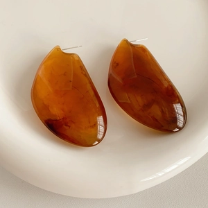 Détails de boucles d'oreilles en résine ambre sur plateau en céramique poli blanc