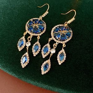 Detail of vintage gold earrings with blue stones on dark green velvet background