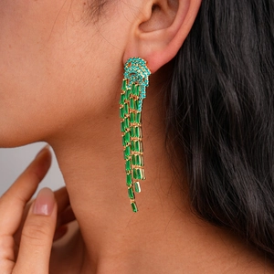 Close-up of golden tassel earrings with emerald green gemstones worn by a model