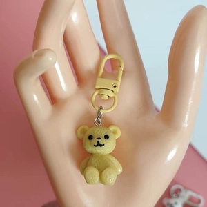Detail view of a yellow resin bear keychain held by a hand model on a split background