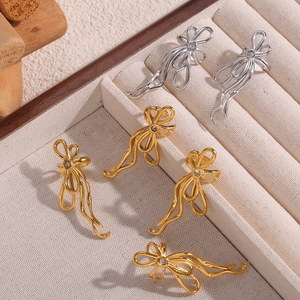 U-shaped bow earrings with zircon stones in gold and silver on a beige jewelry box