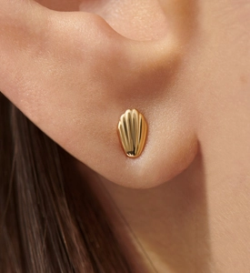 Macro shot of gold shell-shaped stud earrings with textured relief on a model's ear