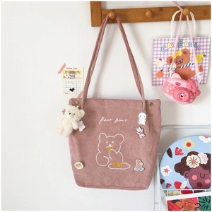 Detail of pink corduroy tote bag featuring bear embroidery and plush charm accessories