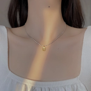 Nahaufnahme einer silbernen Kugelkette mit goldenem quadratischem Anhänger am Model