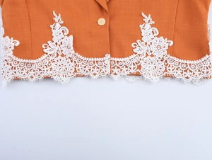 Detail of orange jacket hem featuring intricate white lace trim and a gold button