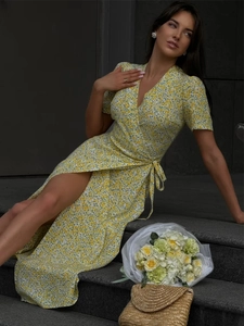 Detailed close-up of yellow floral wrap dress with high slit and waist tie detail