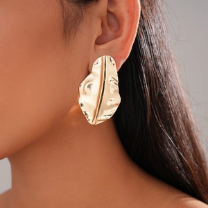Close-up of woman wearing a gold-tone irregular wrinkled leaf earring with metallic texture