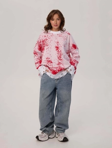 Close-up of distressed pink and white knit sweater with red ink print and ripped cuff detail