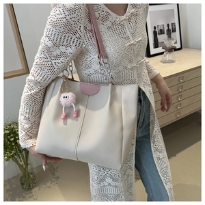 Dettaglio della borsa tote in pelle crema con cinturini rosa e ciondolo di peluche