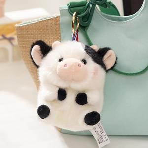 Detail of plush cow keychain with black spots and gold metal ring on a canvas bag