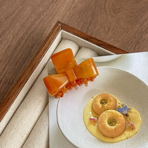 Detail of amber acetate bow hair claw clip with gold lettering on a wooden tray