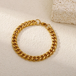 Detailed close-up of golden Cuban link bracelet with lobster clasp on textured surface