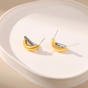 Minimalist gold and silver crisscross geometric stud earrings on a ceramic dish
