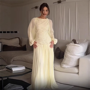 Elegant long sleeve pale yellow pleated maxi dress with waist cinching in a modern home setting
