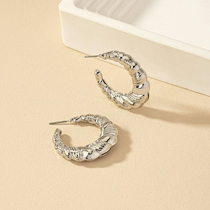 Silver twisted C-shape hoop earrings with a textured glossy finish on a beige background