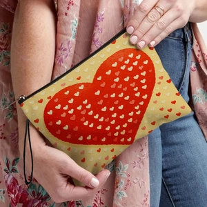 Cosmetic pouch with red heart prints and black wristlet held by a model