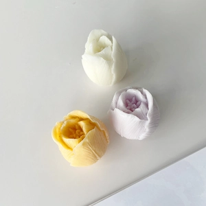 Three tulip-shaped candles in white, yellow, and purple on a minimal white background
