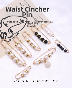Macro detail of 8-piece gold waist tightener pins with pearls and rhinestones on fabric