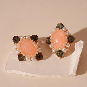 Vintage-Ohrringe mit orange-rosa Steinen und Perlen auf einem Steinständer