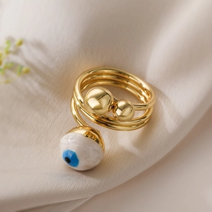 Macro detail of gold-plated spiral ring featuring blue evil eye enamel and gold bead
