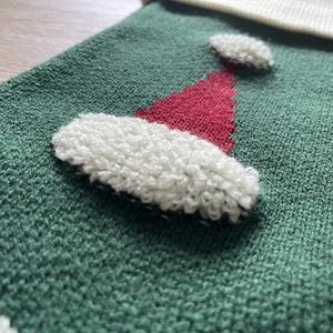 Macro detail of 3D knit Santa hat on green festive Christmas stocking gift bag