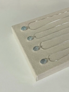 Macro view of four oval aquamarine pendants with S925 silver chains on a textured display