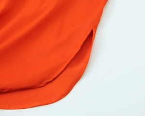 Detail view of orange satin blouse featuring curved hem and side slit design