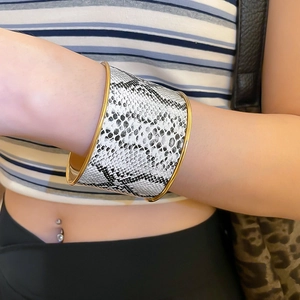 Detail of wide open cuff bracelet with black and white snake skin texture and gold trim