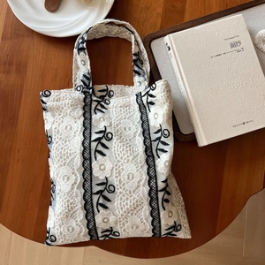 Detail of vintage white lace handbag featuring black floral embroidery on wooden surface