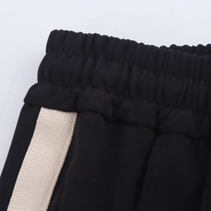 Detailed close-up of black sports trousers featuring an elastic waistband and beige side stripes