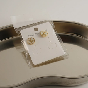 Macro shot of gold stainless steel stud earrings featuring an M letter on branded card
