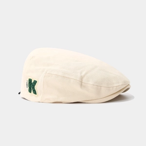 Detailed close-up of beige corduroy kids beret with green letter K patch and fine texture