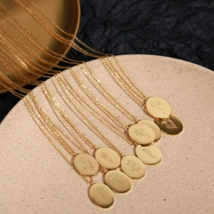 Golden stainless steel oval birth flower necklace displayed on a beige ceramic plate