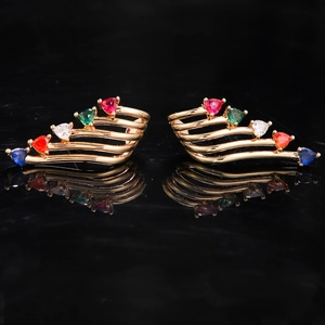 Macro detail of gold-plated wing earrings featuring multi-color heart-shaped gemstones
