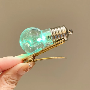 Detail of creative hair clip with glowing green bulb and golden metal alligator clip