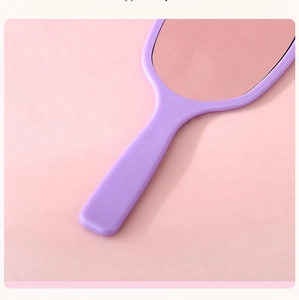 Close-up of a purple handheld vanity mirror with ergonomic handle on pink surface