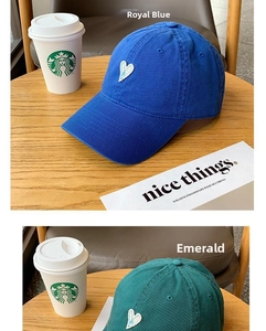 Detailed embroidery of a white heart on cotton baseball caps in blue and green