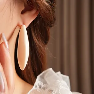 Minimalist white resin teardrop earrings worn by a model in a close-up profile shot