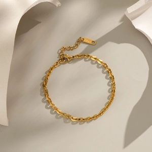 Bracelet chaîne dorée minimaliste avec fermoir mousqueton sur un fond aux tons doux