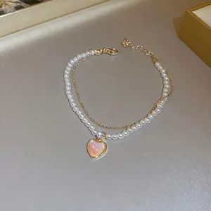 Double-layered gold bracelet with white pearls and a pink heart-shaped pendant