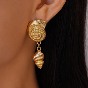 Detail view of gold seashell earrings featuring nautilus stud and conch pendant on model