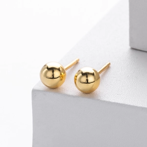 Close-up of high-polish gold ball stud earrings on minimalist geometric white blocks