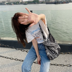 Detailed view of the black paisley canvas tote bag in a casual outdoor riverside setting