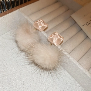 Detail of beige resin square and fluffy fur ball earrings on a soft velvet jewelry box