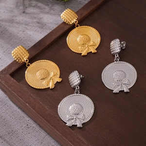 Elegant gold and silver straw hat earrings with textured bows on dark wood tray